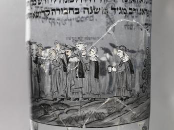 Glass cup etched with Hebrew text and image of group of people walking. 