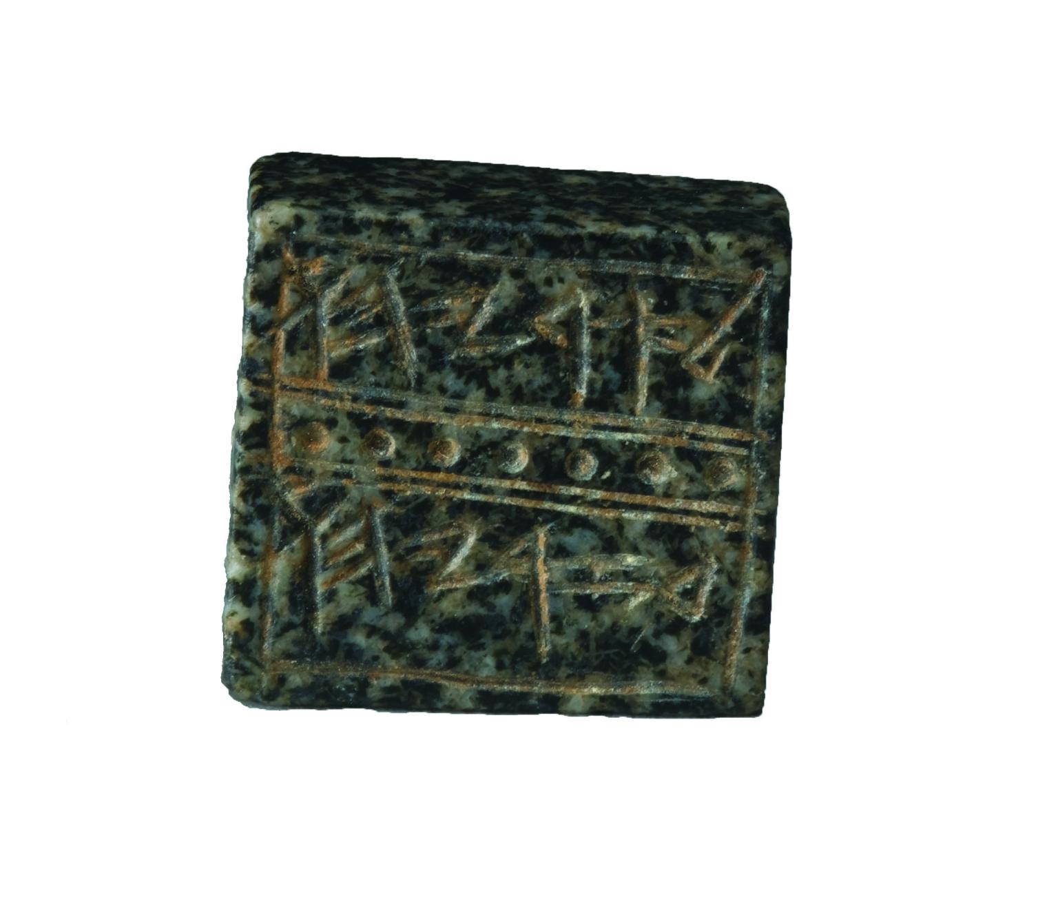 Square rock seal decorated with lines and dots that surround a Hebrew inscription.