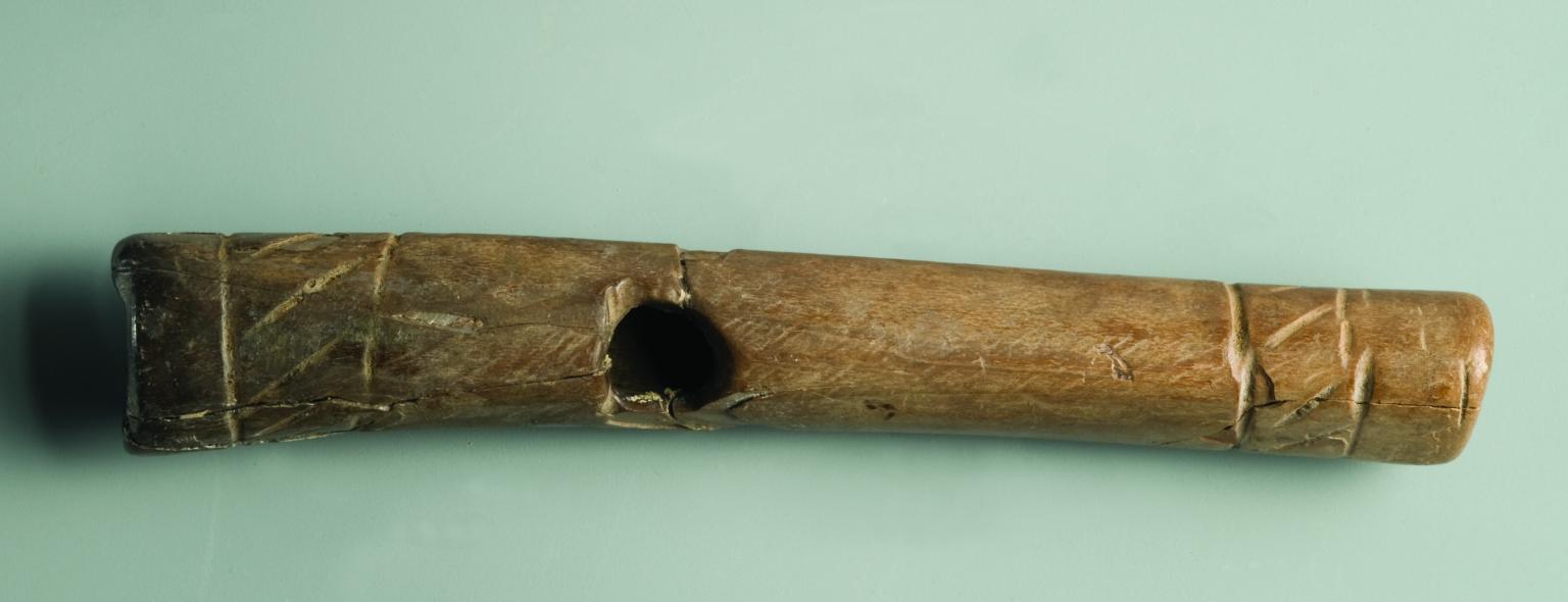 Bone flute decorated with pair of parallel incisions around each end with zigzag design between and hole near center.