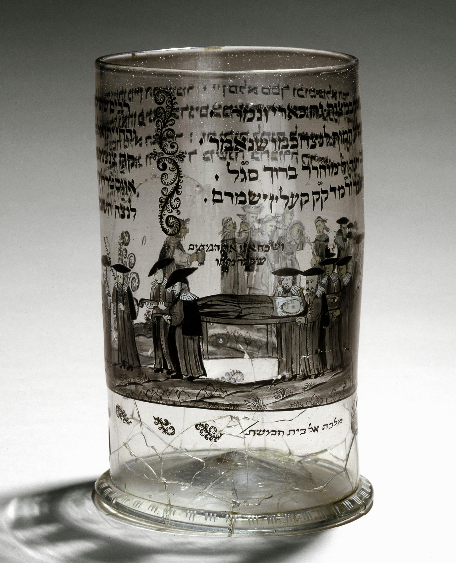 Glass cup etched with Hebrew text and image of people carrying deceased person on stretcher.