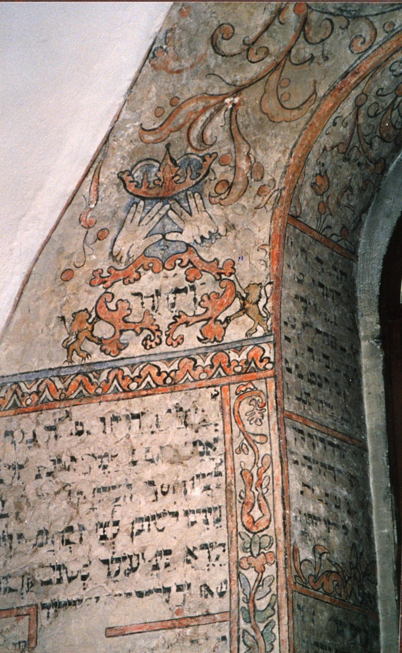 Wall painting with Hebrew text surrounded by floral decorations and two hands beneath a crown.  