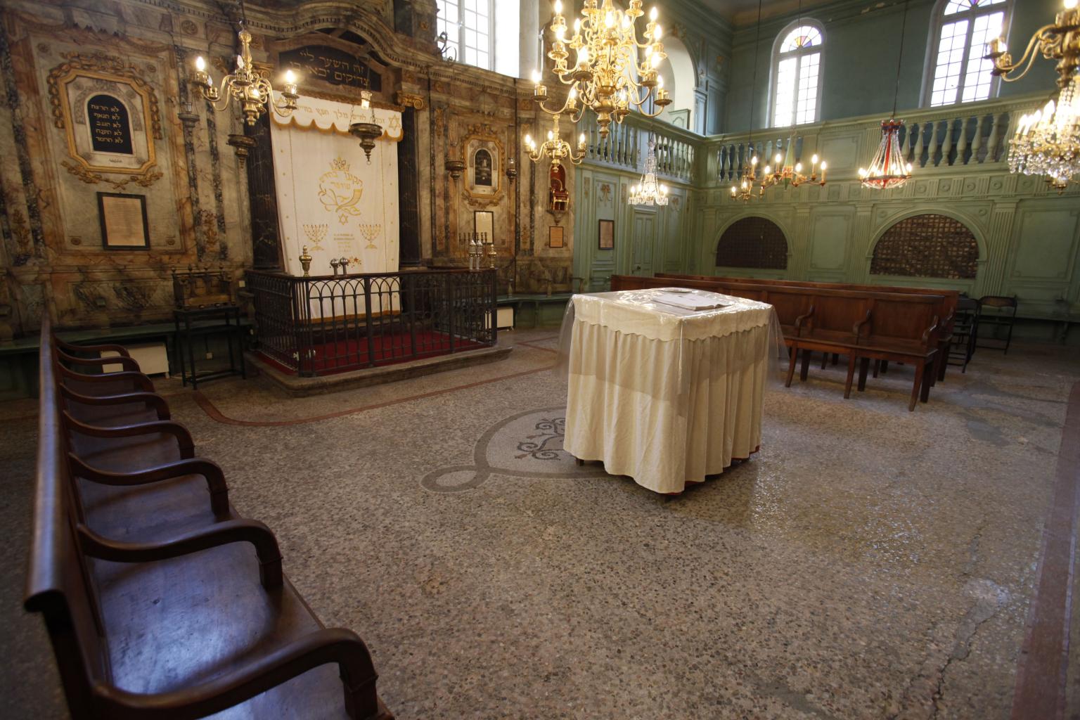 Photograph of room with benches along perimeter of wall and decorated walls, with small central table covered with cloth. 