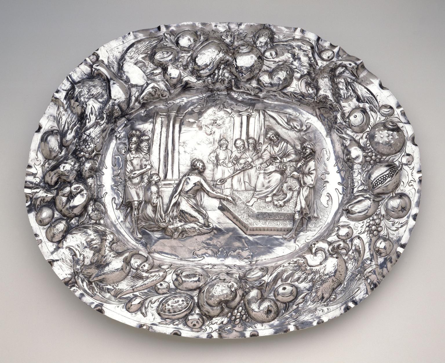 Metal tray with repoussé images of birds and fruit around rim, and image of king and subjects in center. 
