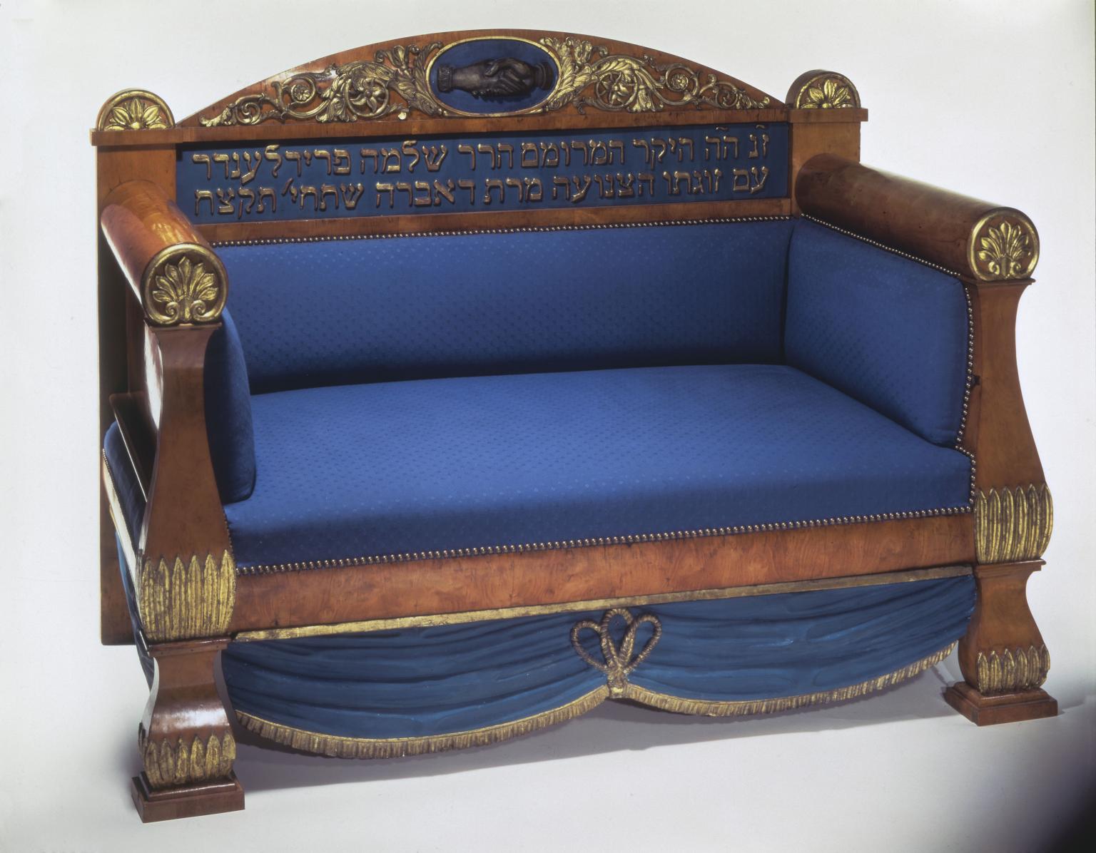 Wooden sofa with upholstered seat, featuring an image of clasped hands and Hebrew inscription on seat back. 