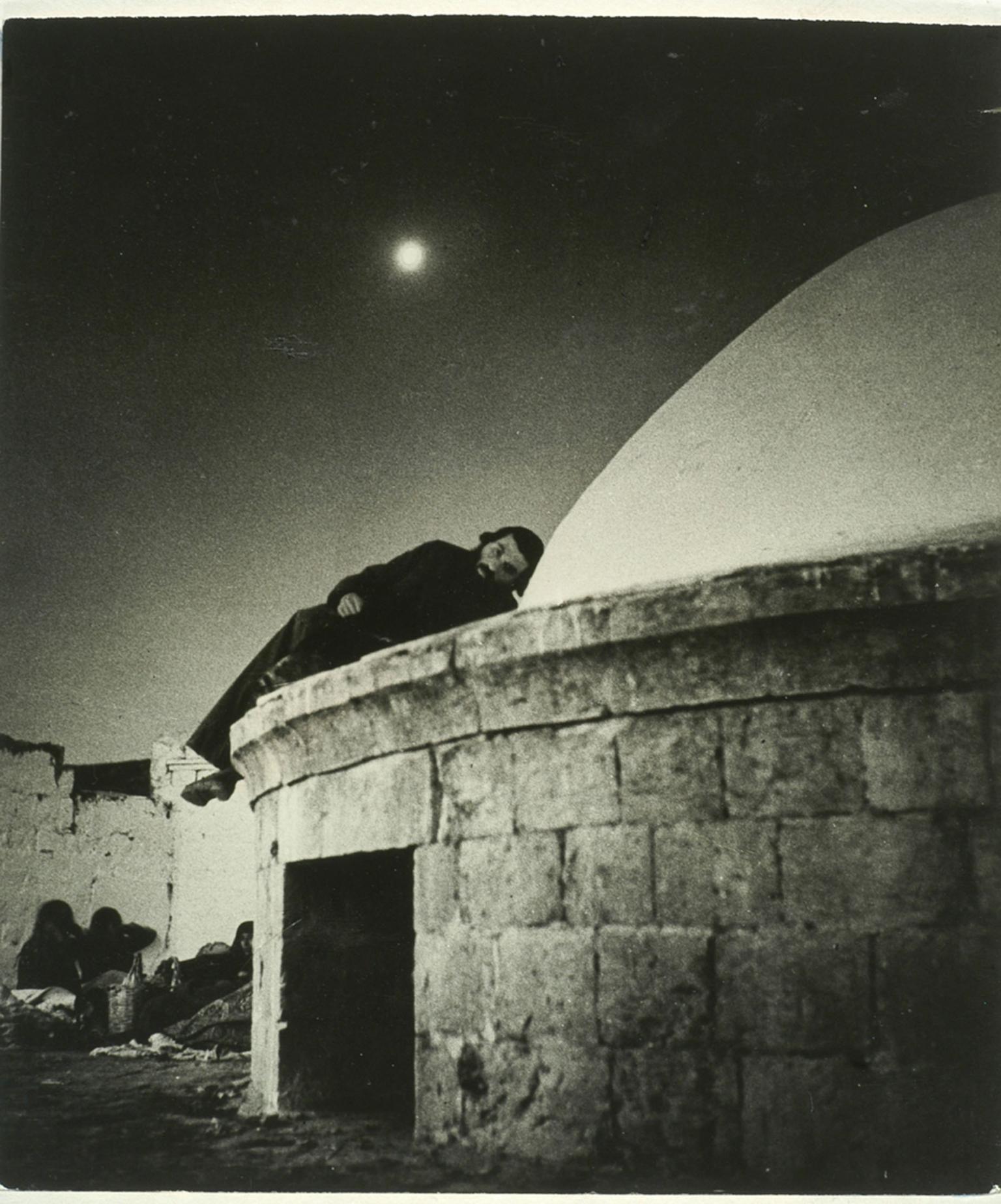 Photograph of man lying on domed roof of stone building.