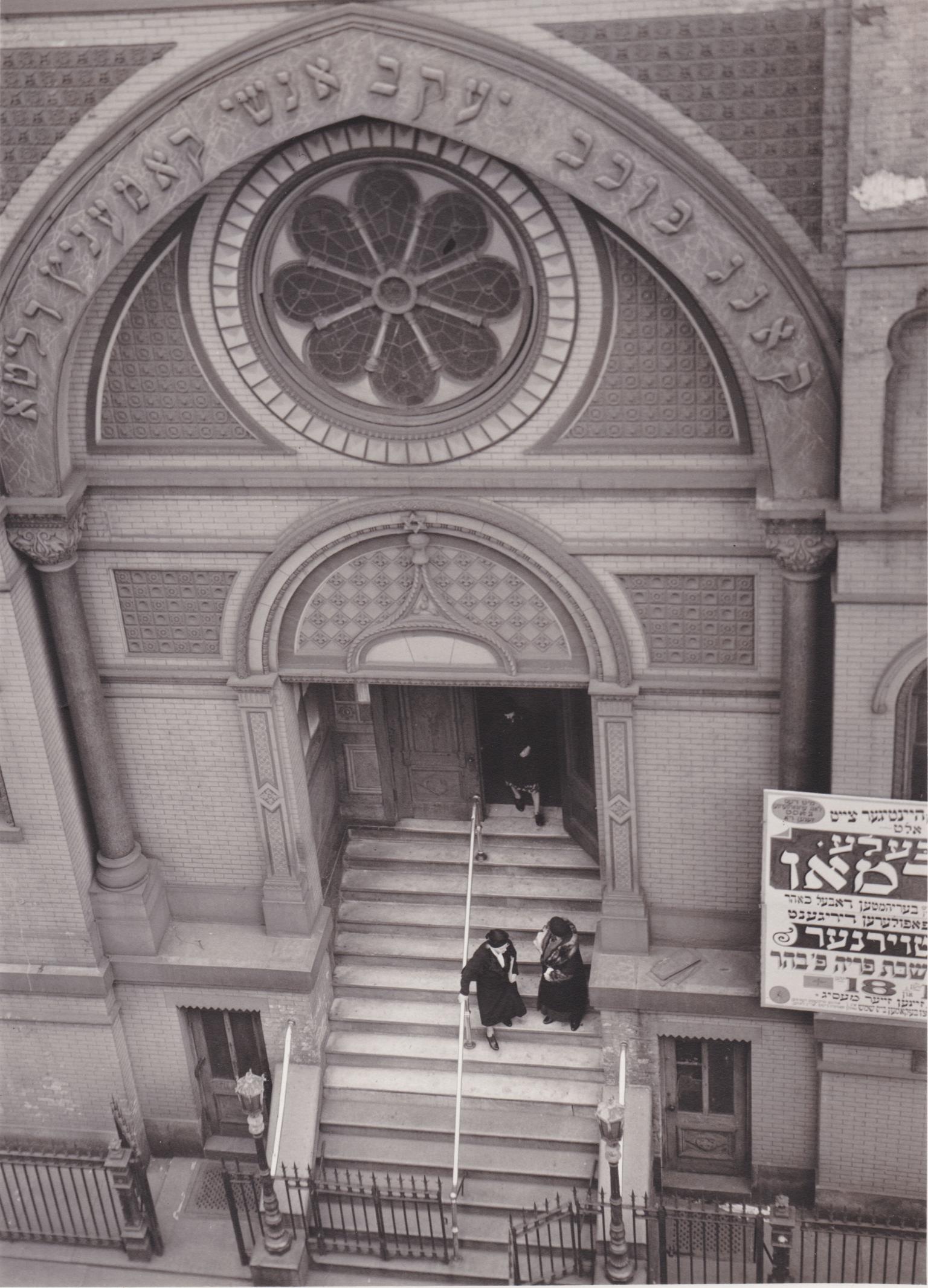 Photograph of building entrance with rose-shaped window and Hebrew inscription seen from above.