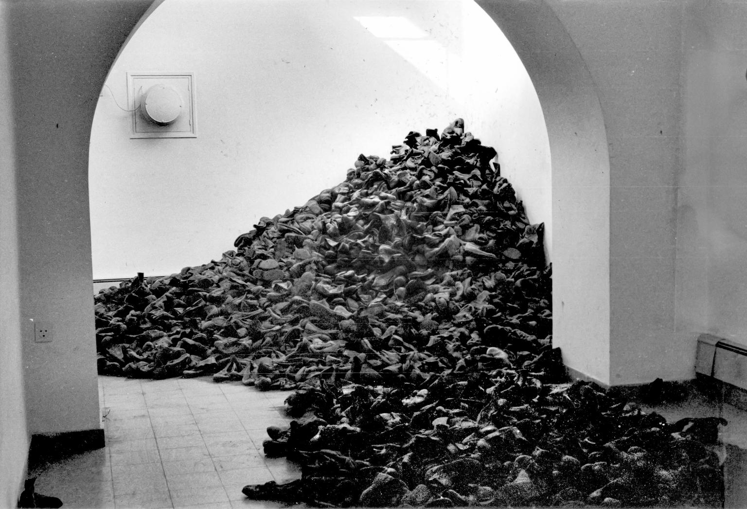 Art installation of large number of boots piled between two rooms.