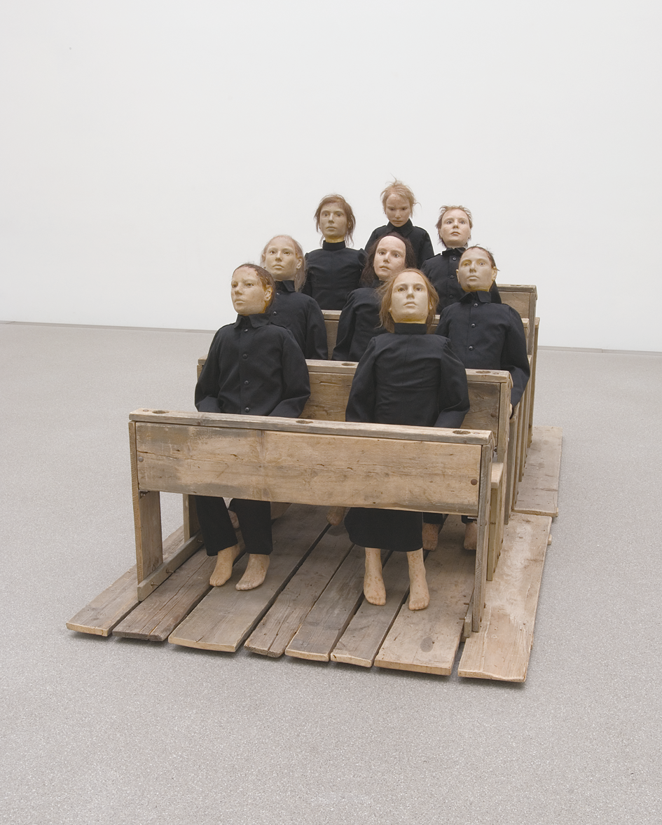 Art installation of eight figures sitting on pews. 