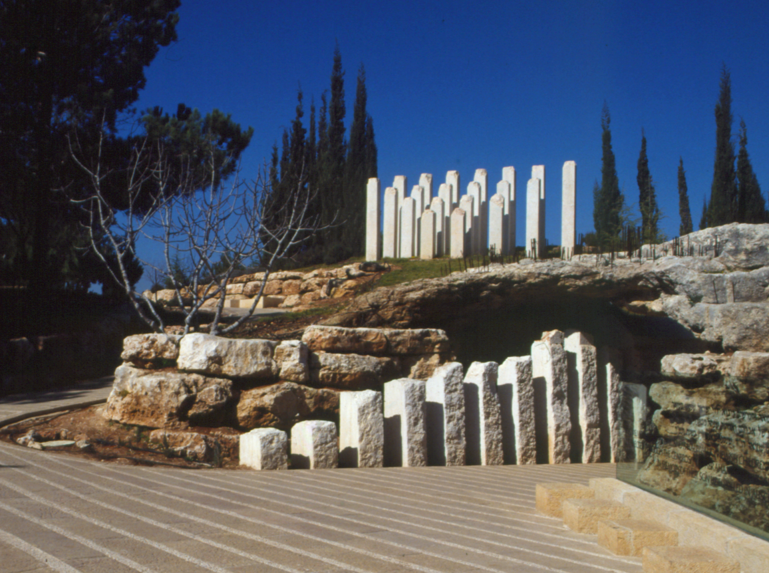 Monument featuring several stelae of different heights set along a rocky cave. 