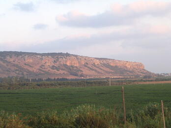 Photo of a red flat-topped mountain with a field of grass in front of it.