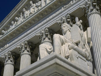 Photo of the United Staes Supreme Court, with a seated figure holding a tablet of law.