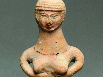 Clay figurine of a woman with a pillar body, arms clasped under her breasts.