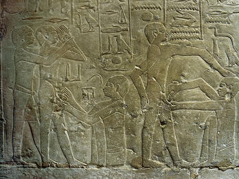 Relief with hieroglyphs above standing figures while others sit and perform circumcisions. 