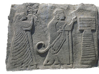 Hittite Couple Sacrificing to Bull Relief with two figures in profile next to podium and bull.