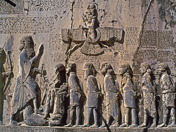 Relief with figures with hands bound standing next to larger figure along wall with relief of winged figure and Persian, Elamite, and Akkadian inscriptions.