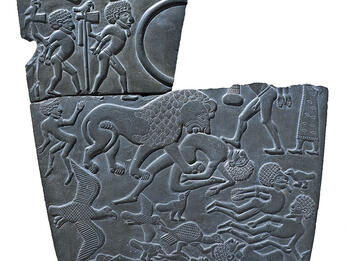 Stone decorated with animals, two figures with hands bound, and floating bodies, cracked on top. 