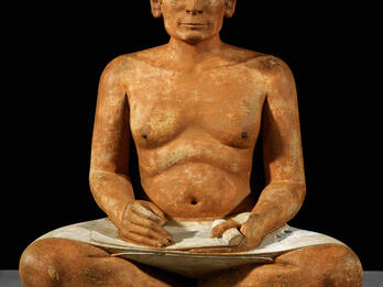 Sculpture of man sitting cross legged with scroll in his lap.