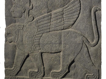 Stone relief of winged lion-like figure with extra head wearing headdress.