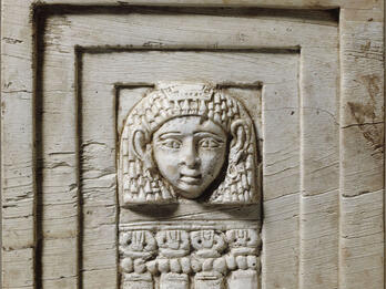 Rectangular relief of face framed in rectangular layers and four small columns below.