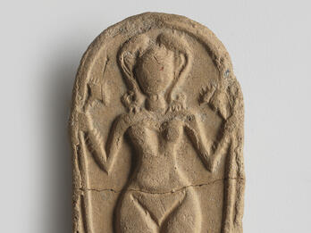 Oval clay piece with figurine of naked woman decorated with headdress, necklace, bracelets, and anklets, and holding a lotus flower.