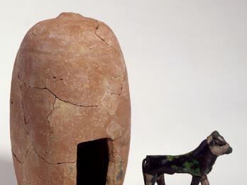 Silver calf figurine next to upright clay building with entrance.