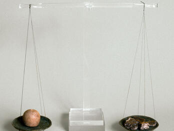 Reconstructed scale with two ancient bronze pans suspended from central beam of clear modern material. The left pan holds a balance weight and the right holds a piece of silver.