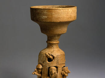 Ceramic stand decorated with carvings of musicians playing instruments.