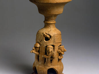 Ceramic stand decorated with carvings of musicians playing instruments.