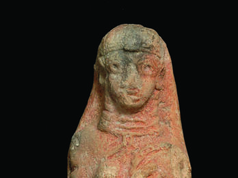 Terra-cotta figurine of woman wearing accessories holding a disk over left breast while right breast is exposed. 