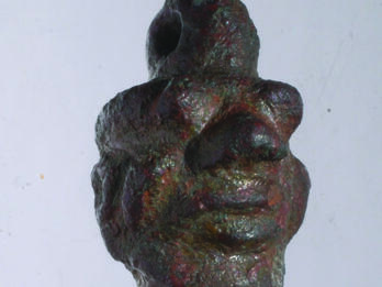 Amulet in the Shape of the Demon Pazuzu Bronze amulet of head with human and animal features and loop on top.