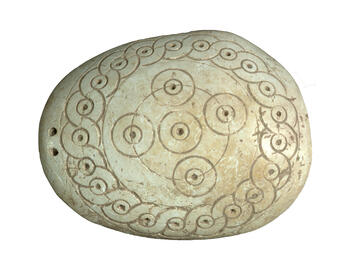 Oval-shaped seashell incised with concentric circles, spirals, and dots in center of circles. 