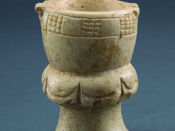 Limestone, goblet-shaped container with a footed base, a midsection with festoon pattern, and a deep bowl with checkerboard pattern on rim.