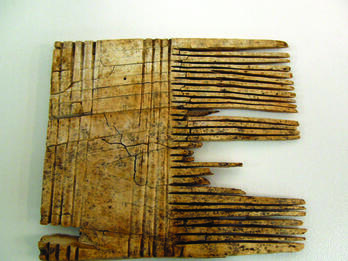 Square-shaped comb with closely-positioned teeth on the right-hand side and wide handle with carved stripes. 