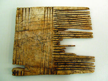 Square-shaped comb with closely-positioned teeth on the right-hand side and wide handle with carved stripes. 