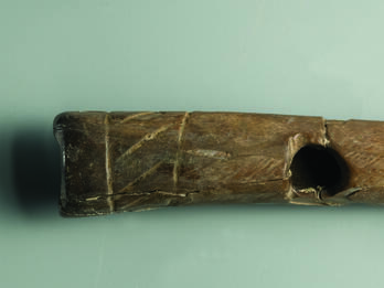 Bone flute decorated with pair of parallel incisions around each end with zigzag design between and hole near center.