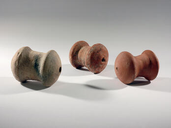 Three spool-shaped terra-cotta objects with a hole on one end.