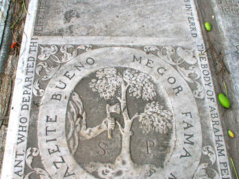 Tombstone with Latin inscription on top half and illustration below of axe chopping tree in half, surrounded by English words around perimeter of stone.