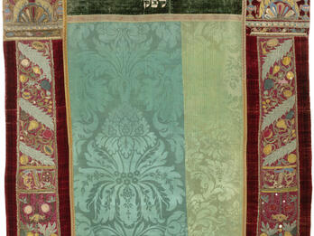 Torah Curtain Embroidered curtain of columns with crowns on left and right sides and decorative floral motifs throughout, and Hebrew text in top center.