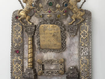 Torah Shield, Dedicated to Sarel bat Moses Tsoref, from Her Husband Shield with decorative border inlaid with semi-precious stones and adorned with lions and crown at top, column on left and plaque in middle with Hebrew text.