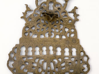 Oil lamp with cut-outs in various shapes, with row of eight cups on bottom and one cup on top. 