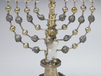 Hanukkah Lamp (Frankfurt am Main) Silver candelabrum with eight branches and a central branch with carved figure on top, and decorative beads on each branch.