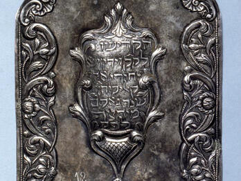 Torah Shield Silver shield of decorative border with Hebrew text in center.