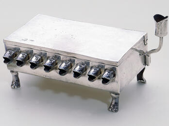 Silver Hanukkah Lamp Silver rectangular lamp with fish-head spouts for the oil and paw-shaped feet.