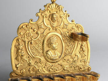 Oil lamp in the form of a shield with spouts at the bottom, of decorative motifs and profile of individual crowned with laurel wreath.