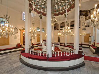 Room interior with central podium with tall columns and many chandeliers surrounding.