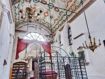 Photograph of room with decorated ceiling, central platform with wrought-iron gate, and bookshelf on far wall.