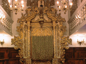 Photograph of room with large carved Torah ark with pews on either side of room and screened second-floor balcony. 