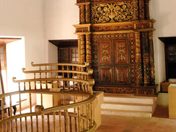 Photograph of room with raised platform with railings in center and carved wooden Torah chamber on back wall.  