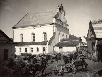 Exterior photograph of buildings on busy street with horses pulling wagons.