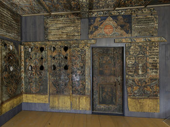 Photograph of room with wood walls painted with Hebrew text, animals, and floral designs.